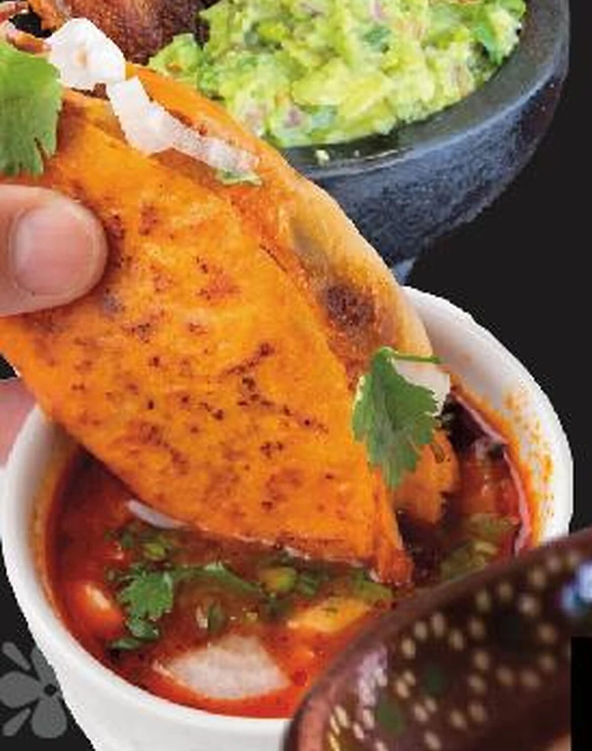 Quesabirria taco de birria de res being dipped into consomé at Goyo Tacos, with guacamole in a molcajete