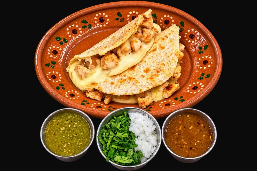 Goyo chicken quesadillas with melted cheese on a clay plate, served with salsa verde, salsa roja, cilantro and onion