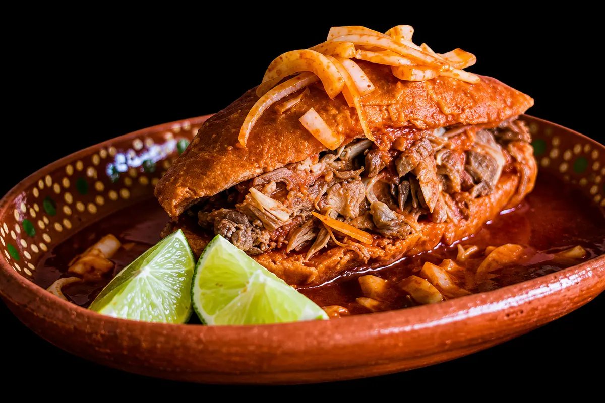 Goyo torta ahogada on birote bread in red chile sauce, topped with pickled onion and served with lime