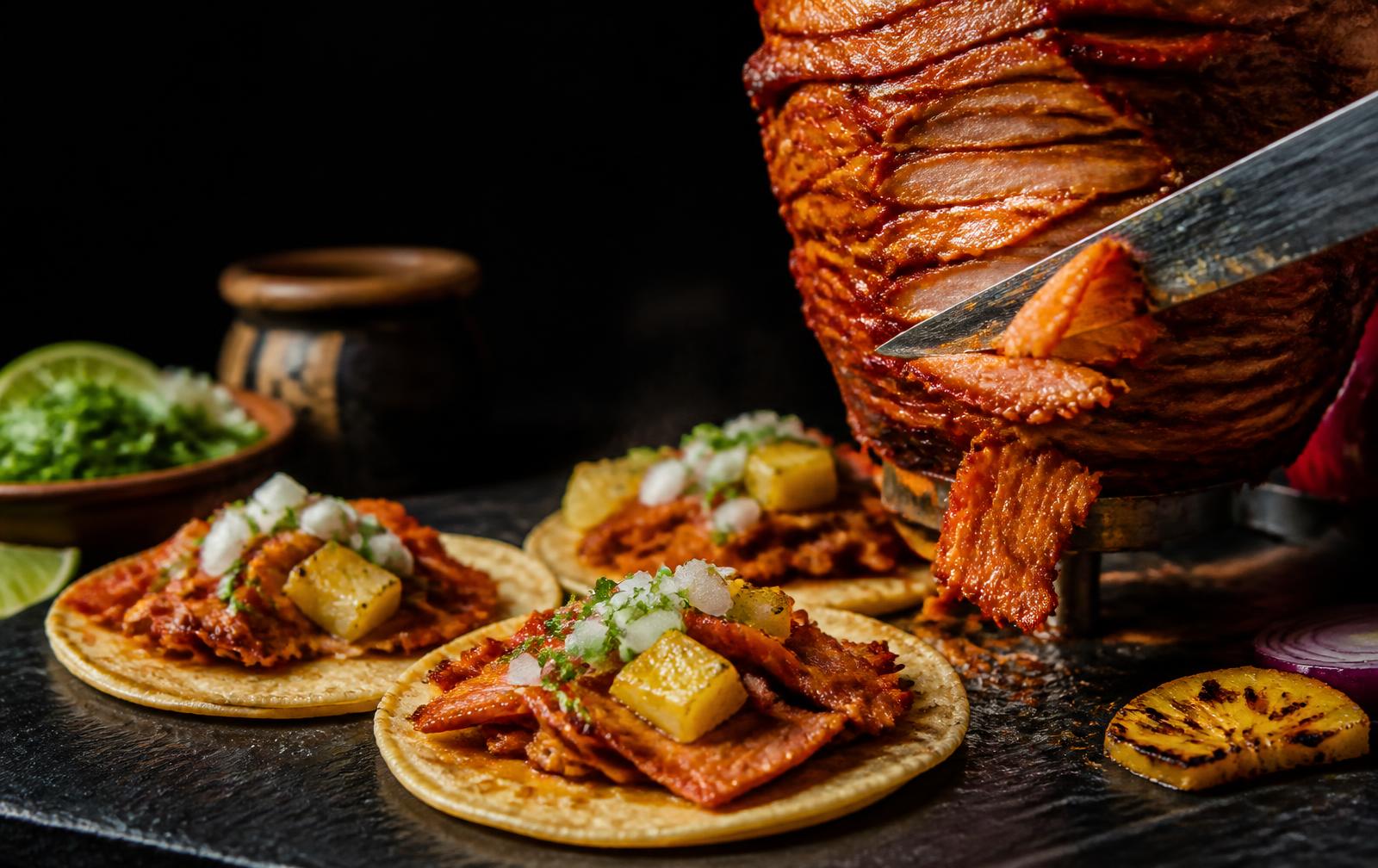 Tacos al pastor with pineapple carved from the trompo